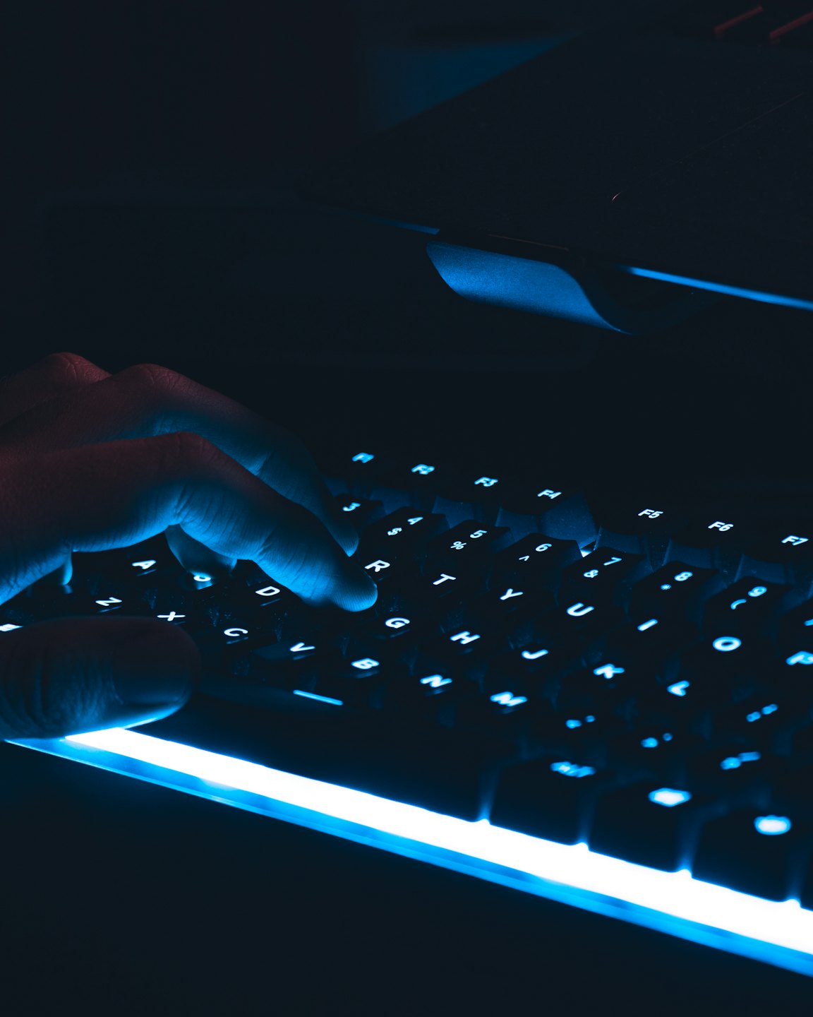 Hand typing on a backlit mechanical keyboard in the dark.