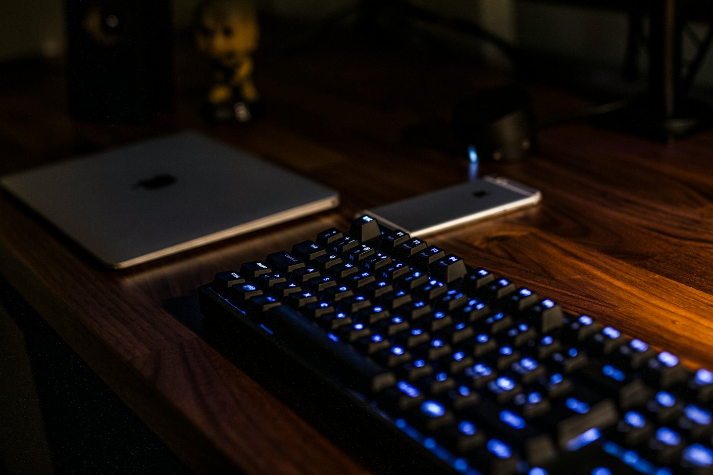 Black mechanical keyboard with blue backlights on a wooden desk.