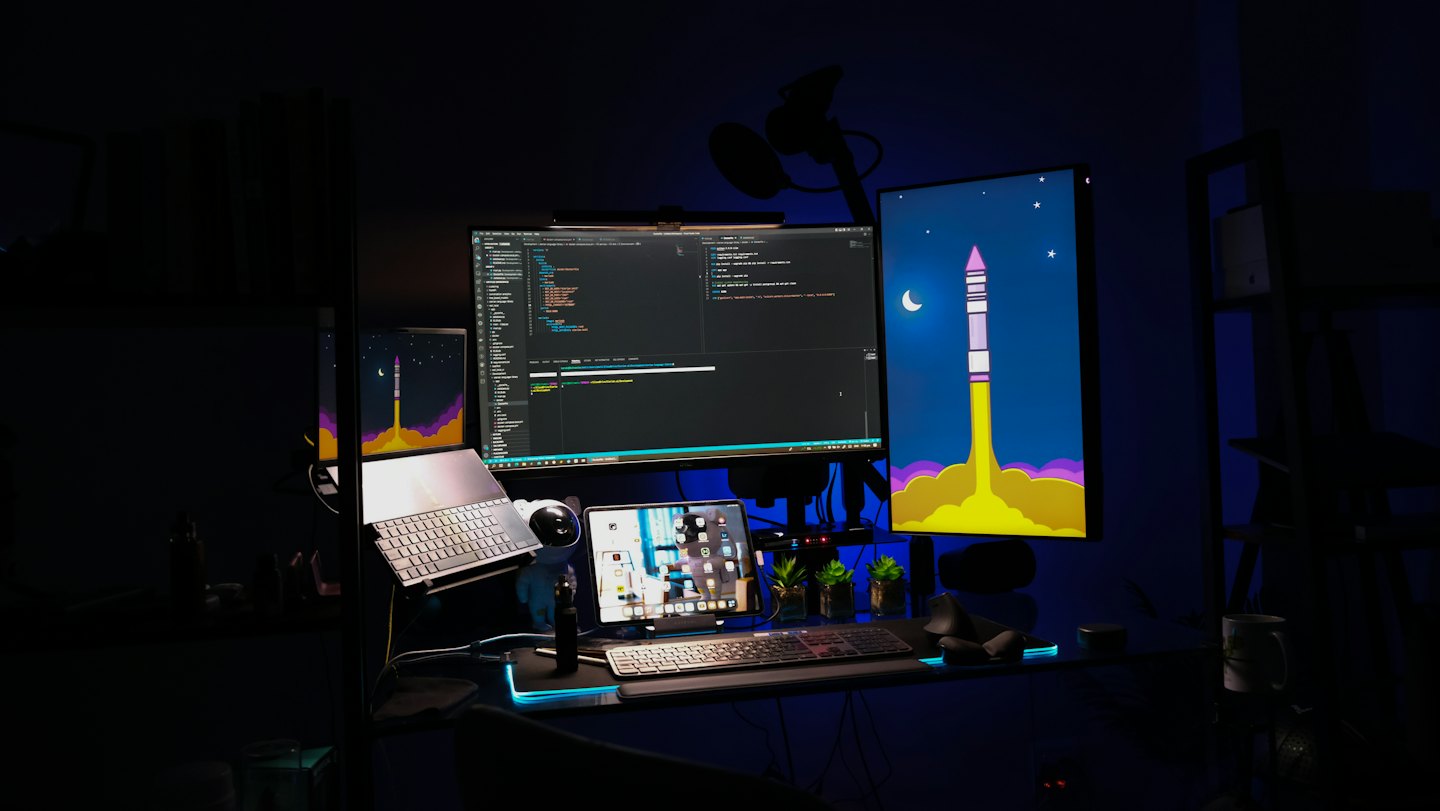 Computer workstation with multiple screens showing code and a rocket launch.